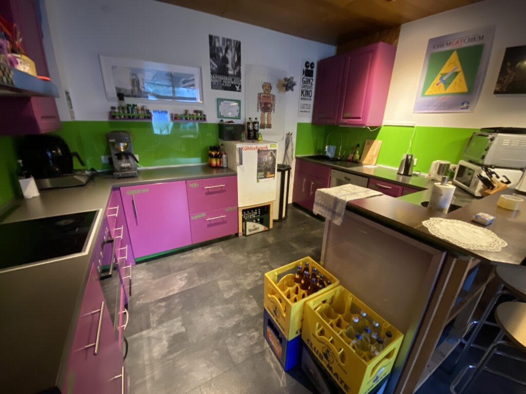 Das Bild zeigt die Küche „Cantina“ im Chaospott. Die Schränke sind violett lackiert. Teile der Wände sind hellgrün gestrichen. 
